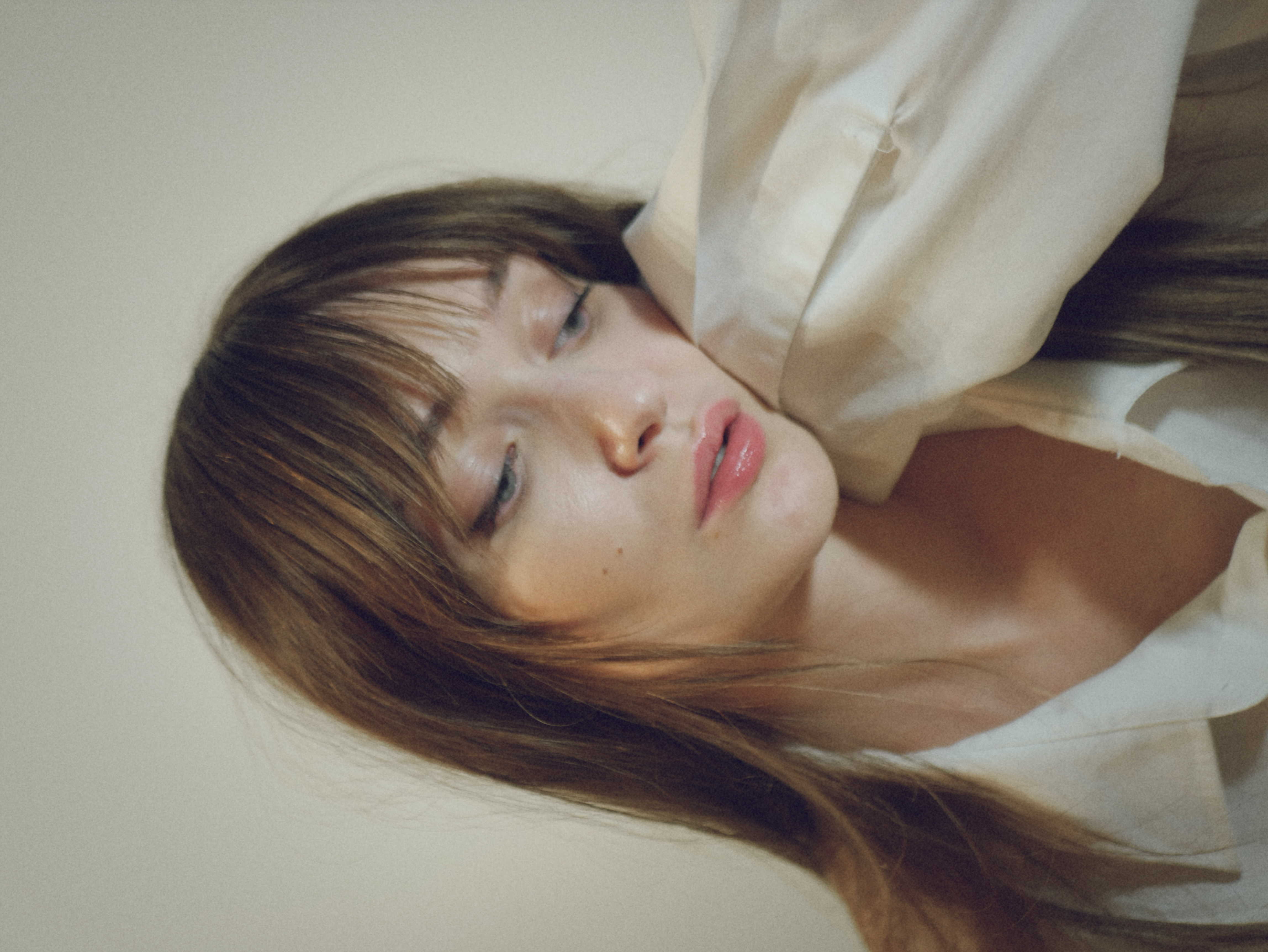 Kris Brouillette resting her head against her sleeve, eyes lowered, in an oversized white shirt